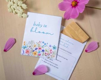 Op de afbeelding: Een witte envelop met de tekst "baby in bloom" en een aquarelbloemendesign. De envelop bevat een klein bruin pakketje met zaden en instructies voor het planten. De instructies omvatten het planten in direct zonlicht en het water geven tijdens droge periodes.