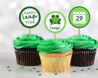 Op de afbeelding: Drie groene cupcakes met groene frosting, bedekt met ronde papieren cupcake-toppers. De toppers tonen een kikker, een kalender met de datum 29 februari en de tekst "Happy Leap Year".