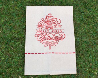 May include: A rectangular off-white fabric pouch featuring red embroidered text that reads Have a Holly Jolly Christmas. The design includes decorative flourishes and a horizontal line of red running stitches across the lower section.