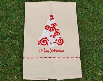 May include: A beige rectangular kitchen towel featuring an embroidered Christmas tree design in red and white swirls. Below the tree, the text Merry Christmas is embroidered in red script, with a horizontal red dashed line near the bottom.