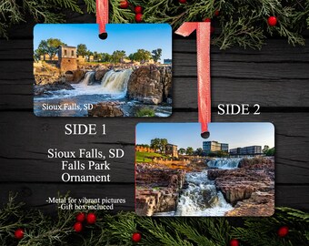 Puede incluir: Adorno rectangular de metal con dos imágenes de Sioux Falls, SD Falls Park. El lado 1 muestra una cascada y un edificio de piedra. El lado 2 muestra una vista diferente de las cataratas. El adorno tiene una cinta roja para colgar.