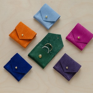 Six wedding ring pouches in suede. Colours include, Clementine Orange, Pale Blue, Ultramarine Blue, Moss Green, Grape Purple and Fuchsia Pink.