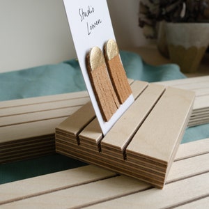 K&ouml;nnte beinhalten: Hellbraune Fransenohrringe mit goldfarbenen Oberteilen, pr&auml;sentiert auf einer wei&szlig;en Karte. Die Karte befindet sich in einem Holzst&auml;nder. Auf der Karte steht der Text "Studio Lowen".