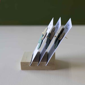 K&ouml;nnte beinhalten: Ohrringe, pr&auml;sentiert auf wei&szlig;en Karten, in einem Holzhalter. Die Ohrringe haben ein blattartiges Design mit goldenen und gr&uuml;nen Akzenten. Der Hintergrund ist ein sanftes Gr&uuml;n.