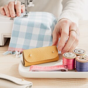May include: A yellow leather key chain with a white plate and spools of thread in pink, white, and blue.