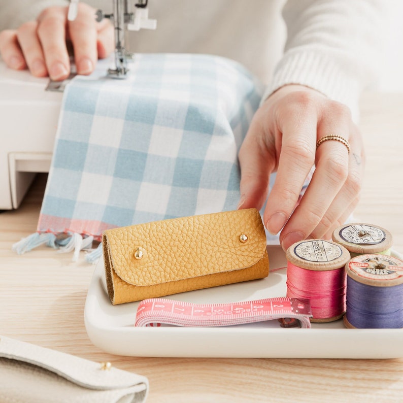 May include: A yellow leather key chain with a white plate and spools of thread in pink, white, and blue.