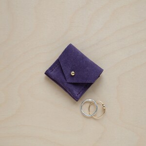 May include: A small purple suede pouch with a gold button closure. Two rings, one gold and one silver, are sitting next to the pouch.