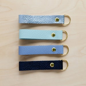 May include: Four leather keychains with gold rings and gold rivets. The keychains are in shades of blue, light blue, and dark blue.