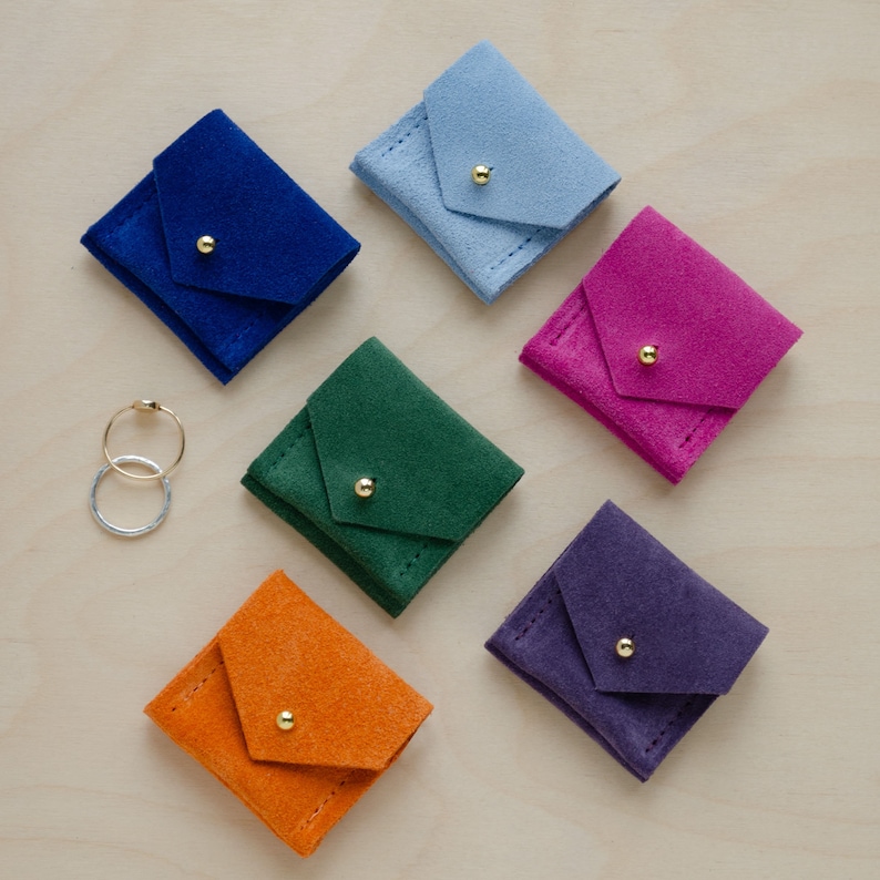 May include: Six small suede pouches in different colors, including blue, green, orange, pink, purple, and light blue. Each pouch has a gold button closure and is ideal for storing small items like jewelry.