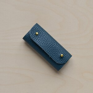 May include: A small, blue leather key holder with two gold metal accents.
