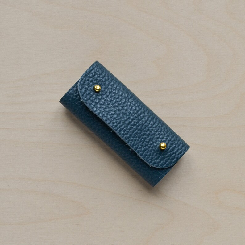 May include: A small, blue leather key holder with two gold metal accents.