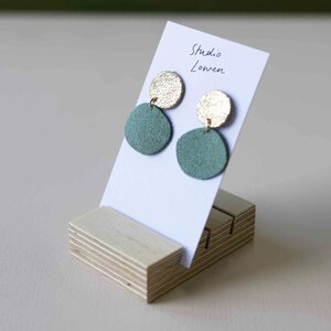 K&ouml;nnte beinhalten: Ohrringe mit einer goldenen Scheibe und einem gr&uuml;nen Wildleder-Kreis. Die Ohrringe werden auf einer wei&szlig;en Karte mit dem Text "Studio Lowen" und einem Holzst&auml;nder pr&auml;sentiert.