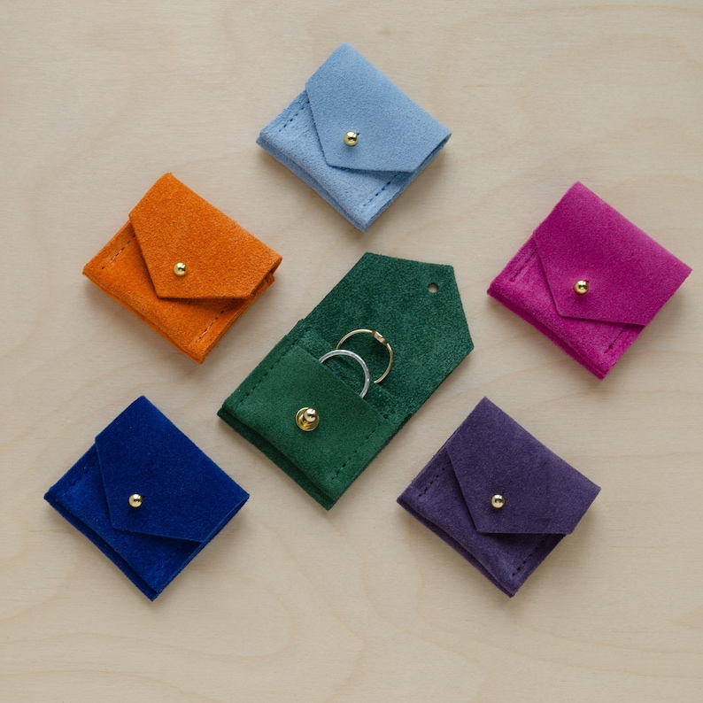 Six wedding ring pouches in suede. Colours include, Clementine Orange, Pale Blue, Ultramarine Blue, Moss Green, Grape Purple and Fuchsia Pink.