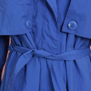 May include: A blue trench coat with a belt tied at the waist. The coat has two buttons on the front.