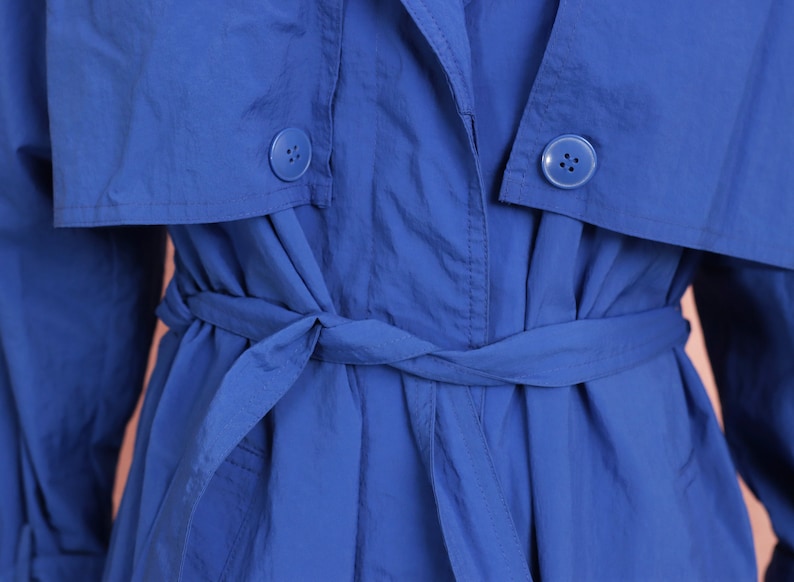 May include: A blue trench coat with a belt tied at the waist. The coat has two buttons on the front.