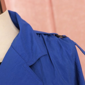 May include: A blue trench coat with a classic collar and a belt. The coat is made of a lightweight fabric and has a relaxed fit.