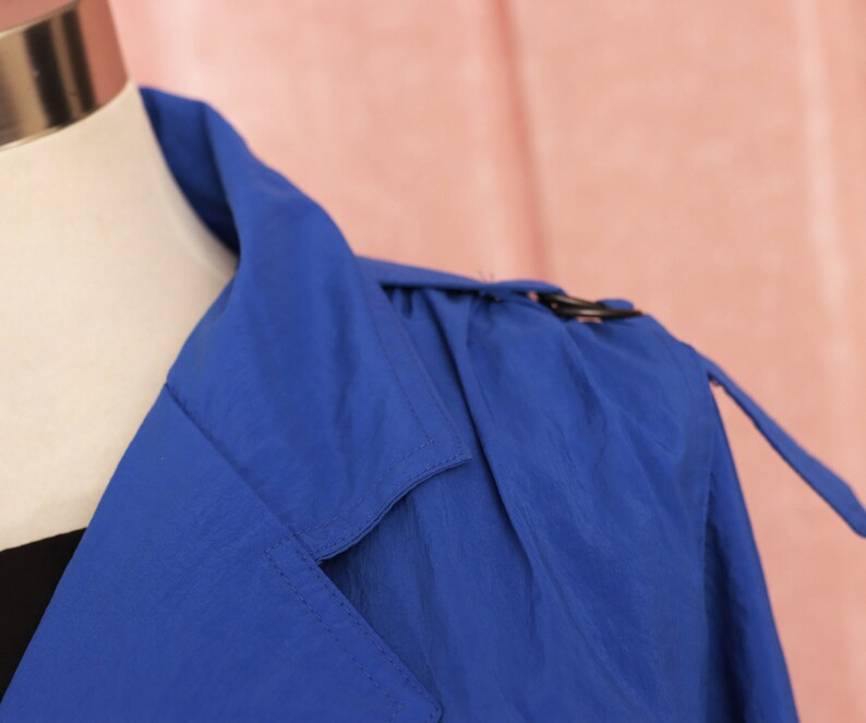 May include: A blue trench coat with a classic collar and a belt. The coat is made of a lightweight fabric and has a relaxed fit.