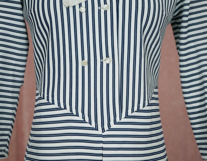 May include: A white and navy blue striped long-sleeved shirt with a double-breasted button closure.