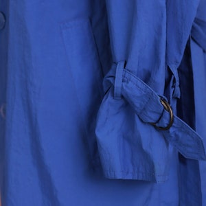 May include: A close-up of a blue jacket with a strap and buckle detail on the sleeve.