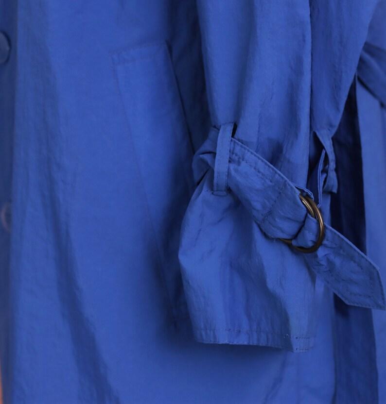 May include: A close-up of a blue jacket with a strap and buckle detail on the sleeve.
