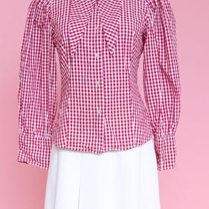 Puede incluir: Una camisa de botones de cuadros rojos y blancos con cuello Peter Pan y mangas largas. La camisa tiene una silueta ajustada y est&aacute; hecha de una tela ligera.