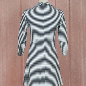 May include: A white and black striped dress with a collared neckline and long sleeves. The dress is fitted at the waist and flares out at the hem.