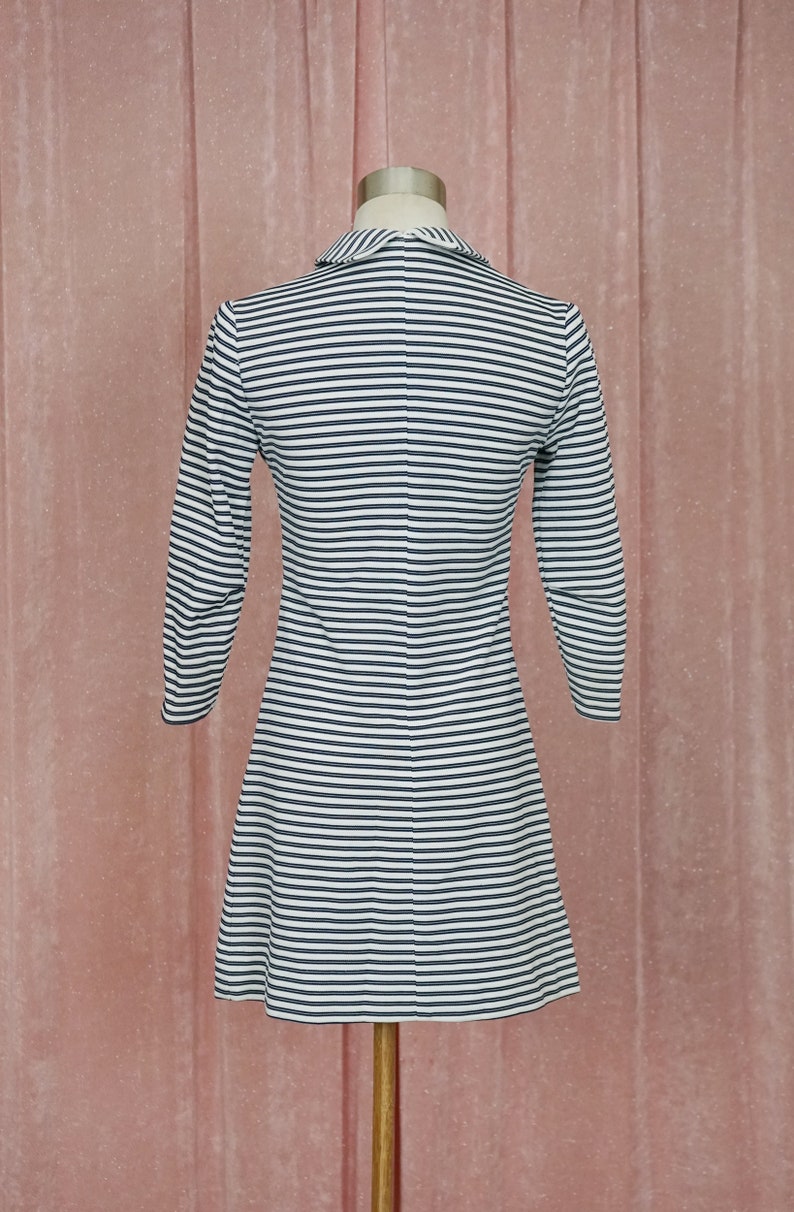 May include: A white and black striped dress with a collared neckline and long sleeves. The dress is fitted at the waist and flares out at the hem.