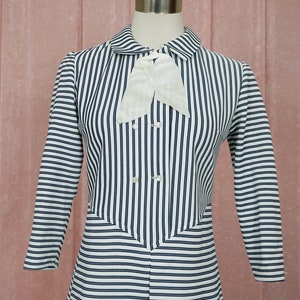May include: A white and navy blue striped dress with a white bow at the collar. The dress has long sleeves and a button-up front.