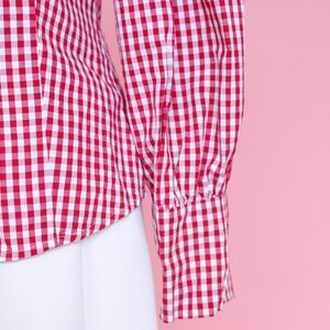 Puede incluir: Camisa de botones de cuadros rojos y blancos con mangas largas y fondo blanco.