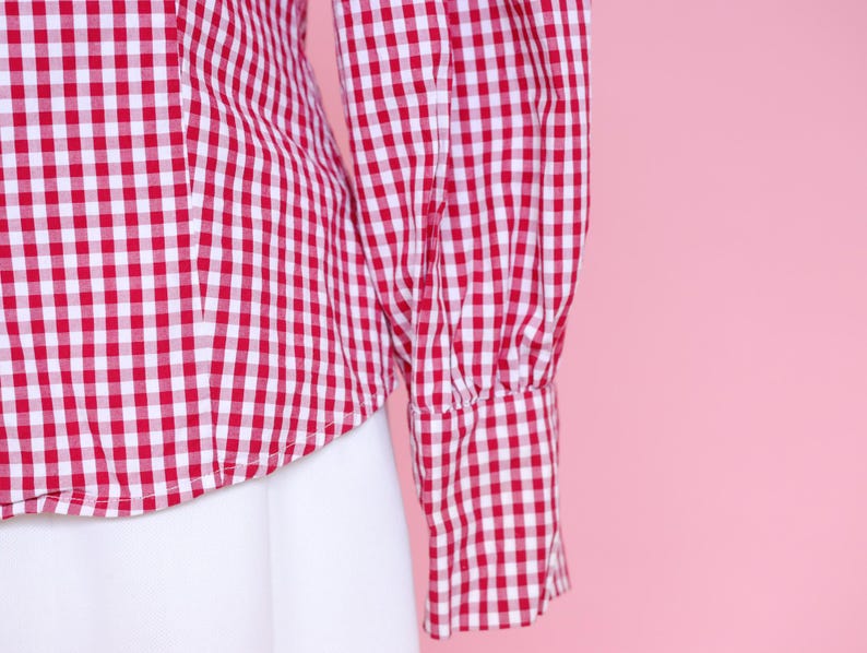 Puede incluir: Camisa de botones de cuadros rojos y blancos con mangas largas y fondo blanco.
