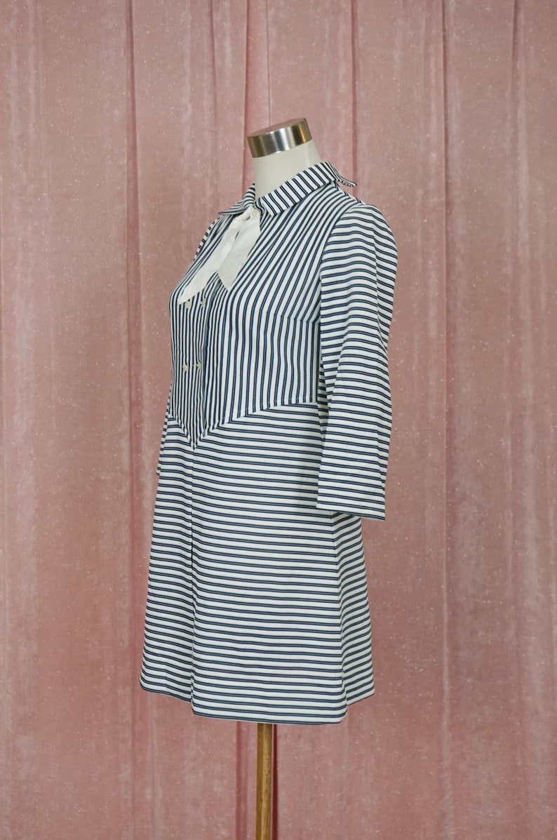 May include: A white and black striped dress with a white bow at the collar. The dress has a button-up front and long sleeves.
