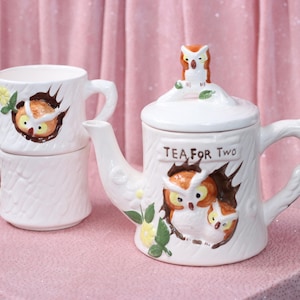 Peut inclure: Théière et deux tasses en céramique blanche avec des motifs de hiboux. La théière a un couvercle avec un hibou sur le dessus et le texte "Tea for Two" sur le côté. Les tasses représentent des hiboux qui sortent de troncs d'arbres.