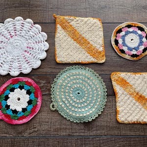 May include: A collection of six handmade crochet items, including round and square pot holders and coasters. The items feature various colors, including white, beige, pink, blue, and orange. The designs include floral patterns and diagonal stripes.