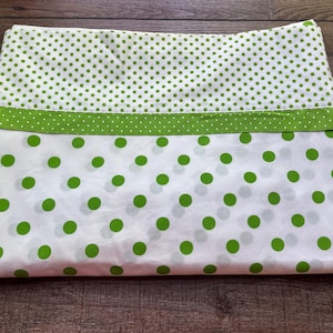 May include: A white pillowcase featuring a pattern of bright green polka dots. The top section has smaller, densely packed dots, separated by a solid green band from the lower section, which displays larger, more widely spaced green dots.