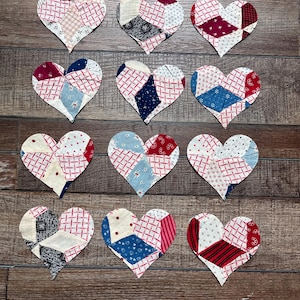 May include: Twelve heart-shaped fabric ornaments arranged in a grid. Each heart is constructed from multiple patches of cotton fabric featuring various patterns including red and white grids, blue floral prints, and solid black, red, and white sections.
