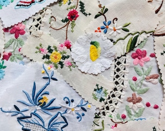 May include: A collection of white fabric scraps featuring various colorful floral and butterfly embroidery designs. The pieces include scalloped edges, intricate needlework in shades of blue, pink, red, and yellow, and delicate lace trim details.