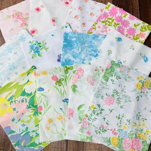 May include: A collection of twelve square fabric swatches featuring various floral and abstract patterns in shades of pink, blue, yellow, green, and white. The pieces are arranged in a grid-like pattern, showcasing diverse botanical prints.