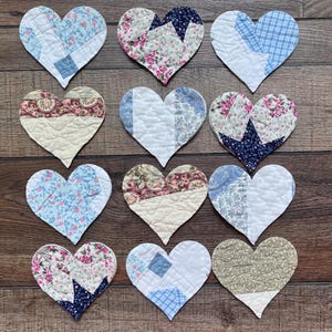 May include: A collection of twelve heart-shaped fabric coasters featuring various patchwork designs. The quilted hearts display a mix of floral, plaid, and solid patterns in shades of blue, pink, cream, and green, each with visible stitching.