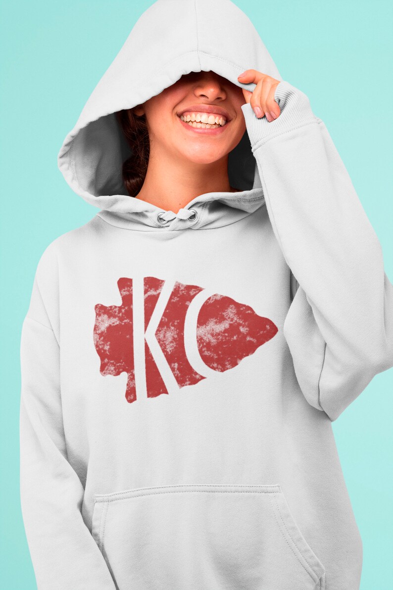 May include: White hoodie with a red distressed arrowhead design featuring the letters "KC" in white.