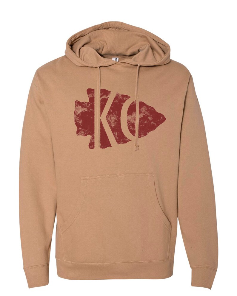 May include: A tan hoodie with a red distressed arrowhead graphic featuring the letters "KC" inside.