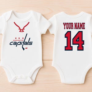 Könnte beinhalten: Weißer Baby-Body mit dem Washington Capitals Logo auf der Vorderseite und der Nummer 14 auf der Rückseite. Die Vorderseite zeigt ein rot-blaues Hockey-Design. Auf der Rückseite steht "YOUR NAME" über der Nummer 14.