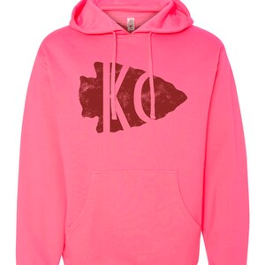 May include: A pink hooded sweatshirt with a red distressed arrowhead graphic featuring the letters "KO" inside.