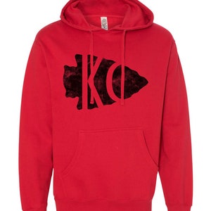 May include: Red hooded sweatshirt with a black velvet arrowhead design featuring the letters "KC" inside.