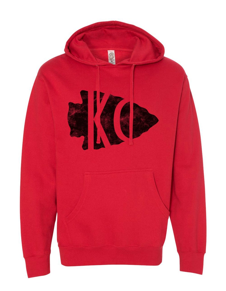 May include: Red hooded sweatshirt with a black velvet arrowhead design featuring the letters "KC" inside.
