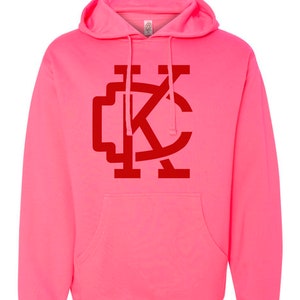 May include: A pink hoodie with a red "KC" logo on the front.