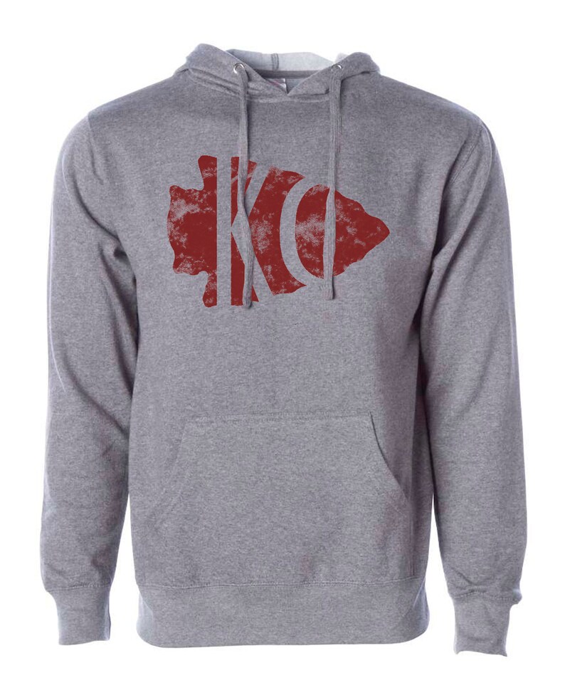 May include: A gray hooded sweatshirt with a red distressed arrowhead design featuring the letters "KC" inside.