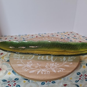 May include: A long, narrow, leaf-shaped glass tray featuring a gradient of deep green at the edges transitioning to a bright yellow-green in the center. The surface has a textured, ribbed pattern mimicking the veins of a tropical palm leaf.