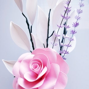 May include: A pink paper rose with white paper leaves and purple paper flowers.