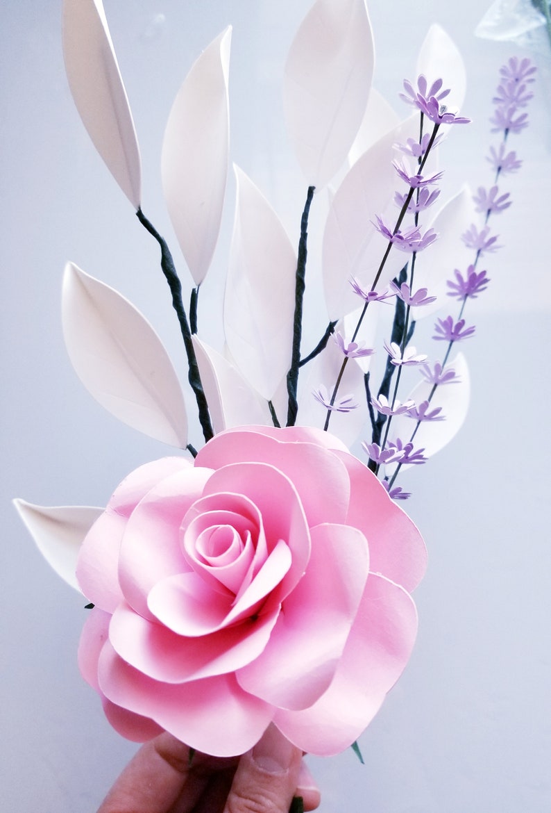 May include: A pink paper rose with white paper leaves and purple paper flowers.