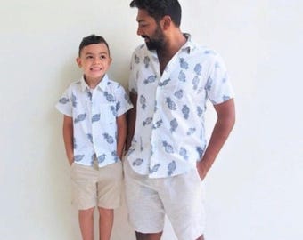 Könnte beinhalten: Zwei Personen tragen weiße Hemden mit kurzen Ärmeln und einem blauen Ananasdruck. Die Person links ist ein Kind, das eine Khaki-Shorts trägt. Die Person rechts ist ein Erwachsener, der eine beige Shorts trägt.